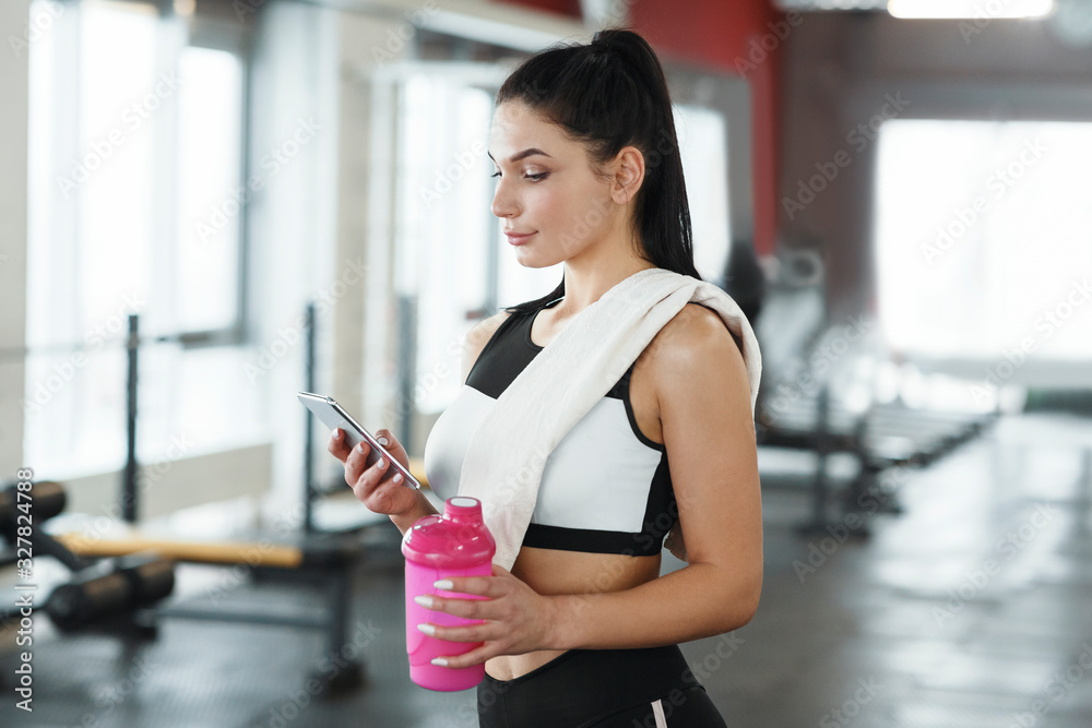 © Prostock-studio - Young woman with smartphone and bottle of water or protein shake in gym