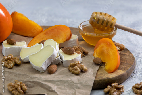 Brie and persimmon cheese with almonds and walnuts on a wooden Board and a gray background. Honey in a glass bowl.Close up