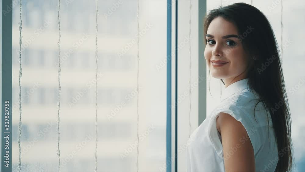 Attractive businesswoman is looking out the window and then is looking at the camera, with a wide smile. Close up. Copy space. 4K. Attractive businesswoman is looking out the window and then is looking at the camera, with a wide smile. Close up. Copy space. 4K.