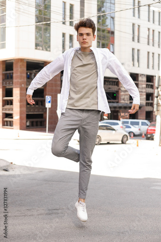 guy model with a stylish haircut posing outdoors in a white shirt and gray trousers. trendy hairstyle rests near a modern business center. Attractive guy in the street on a summer day.
