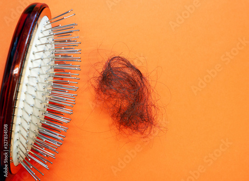 Comb and fallen female hair close-up with copy space on an orange background, top view.