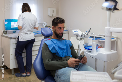 Male patient being looking at the smartphone while the female dentist prepares to work.