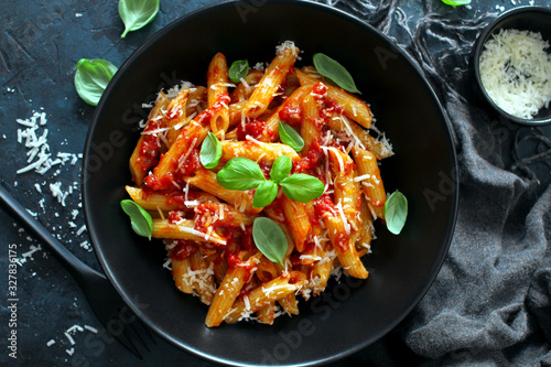 Penne pasta with tomato sauce  parmesan cheese and basil on dark background. Top view with copy space.