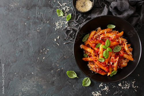 Penne pasta with tomato sauce, parmesan cheese and basil on dark background. Top view with copy space.