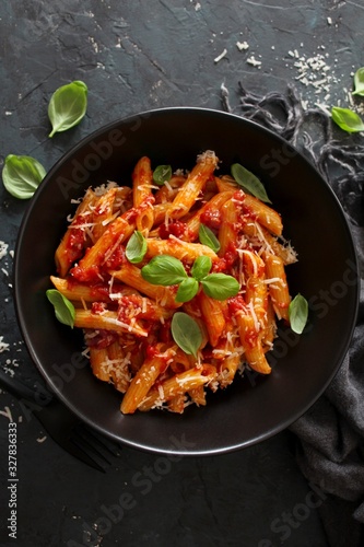 Penne pasta with tomato sauce, parmesan cheese and basil on dark background. Top view with copy space.