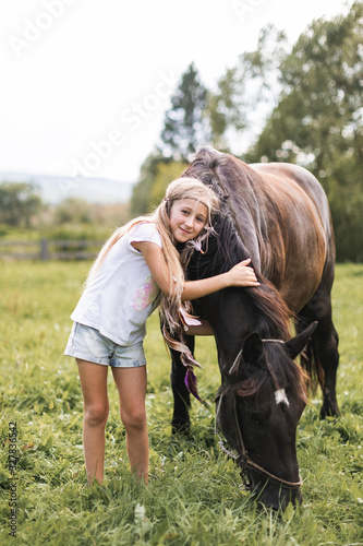 Ranch, countryside, nature. Lovely girl with horse. Pretty girl with blond long hair touching and petting beautiful horse outdoor at nature.
