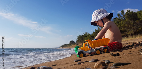 a little boy playing with toy truck and shovel on the beach on a hot summer day
