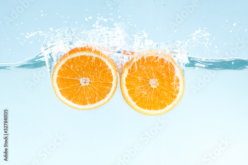 Yummy juicy orange cut in half and water splashes on blue background