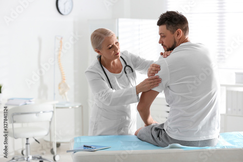 Male orthopedist examining patient's arm in clinic photo