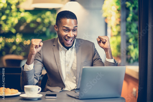 Excited black man celebrating his victory at the cafe