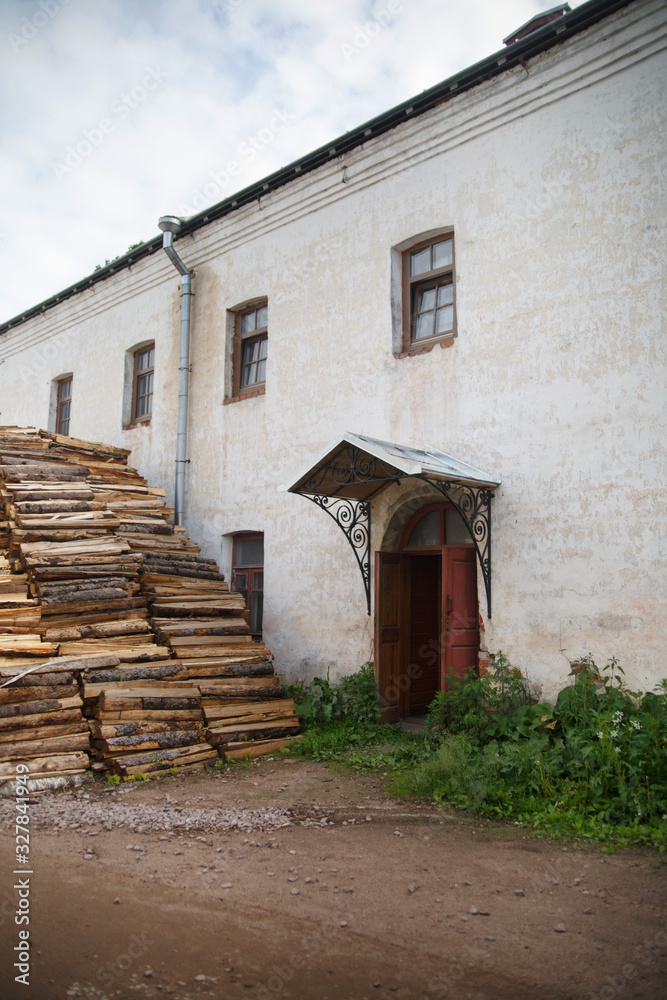 A large pile of firewood lies in the yard near an old house on a summer morning in the countryside.