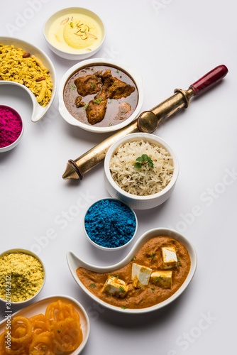 Happy Holy concept  showing Indian assorted lunch food like chicken, paneer butter masala, naan, jeera rice, black chana fry, jalebi, fujiyama, thandai and Farsan with holi colours and pichkari  photo