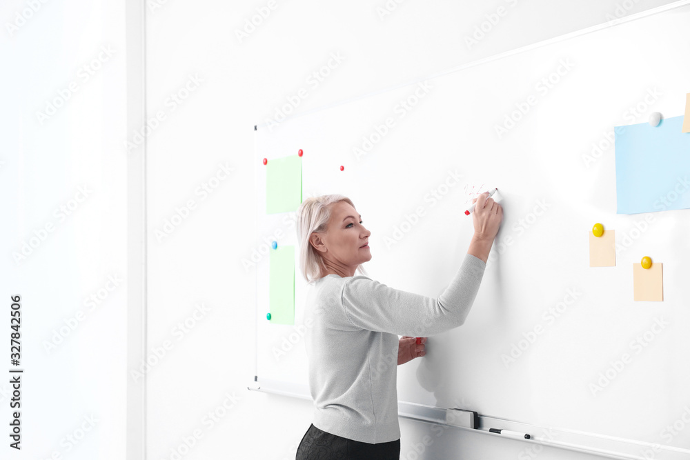 Fototapeta premium Mature teacher writing on whiteboard in classroom