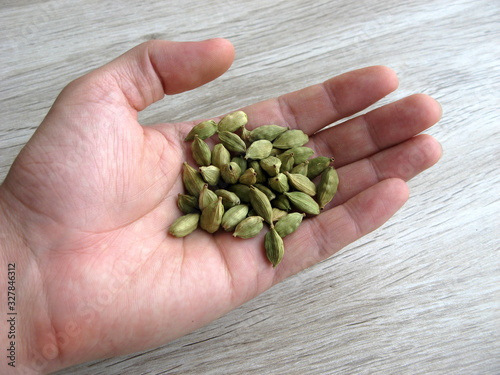 Close up of green cardamon seeds on male hand with wooden background.