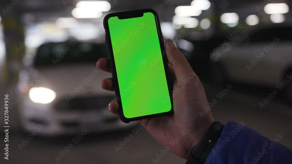 Lviv, Ukraine - May 19, 2018: Hands holding phone with vertical green screen in the background moving car flashing bonnet is raised man chroma key technology use mobile internet message smart sunlight