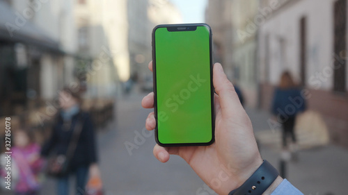 Lviv, Ukraine - May 19, 2018: In city center man hands holding use touch phone with horizontal green screen street background sunset busy finger touch message cellphone display girl slow motion