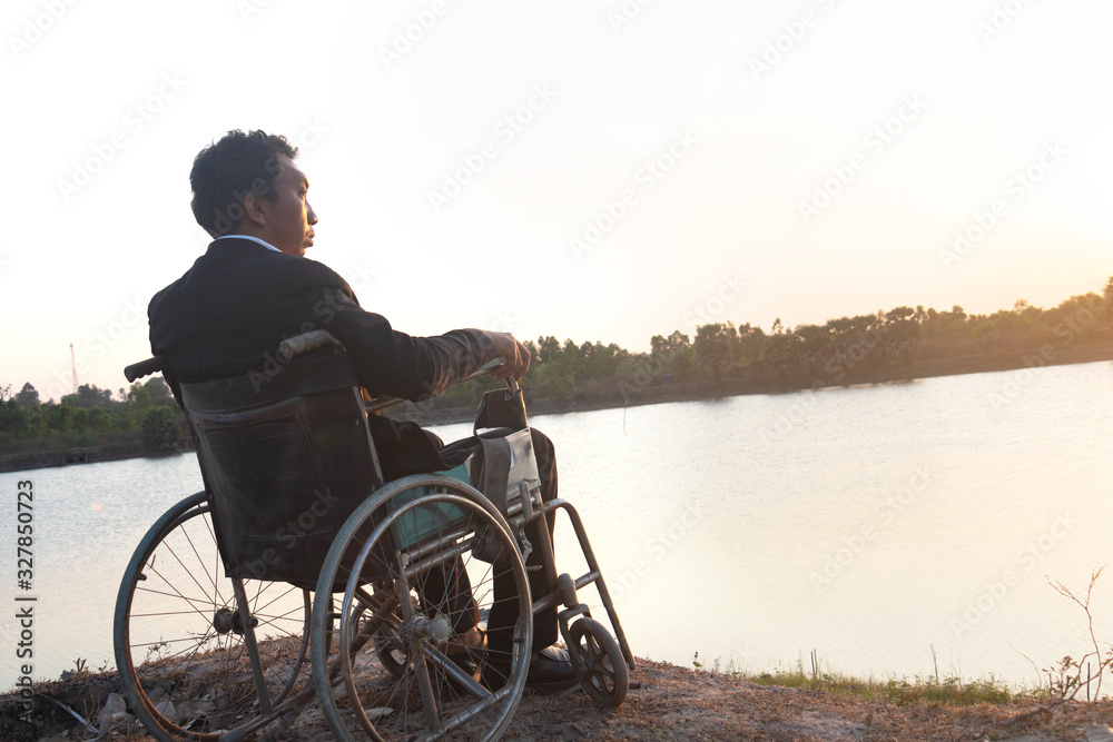 Young disabled man with blue sky background.He is alone and sitting on wheelchair.He is looking into river.despair,lonely,hope.Photo concept depression and Patient.