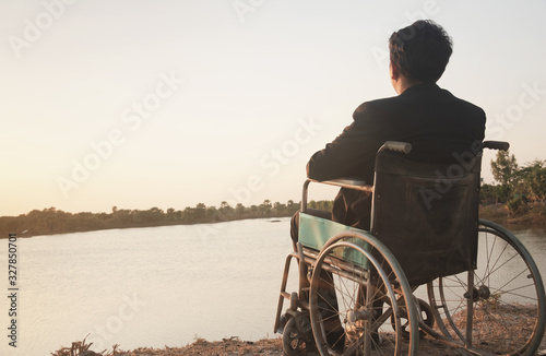 Young disabled man with blue sky background.He is alone and sitting on wheelchair.He is looking into river.despair,lonely,hope.Photo concept depression and Patient.