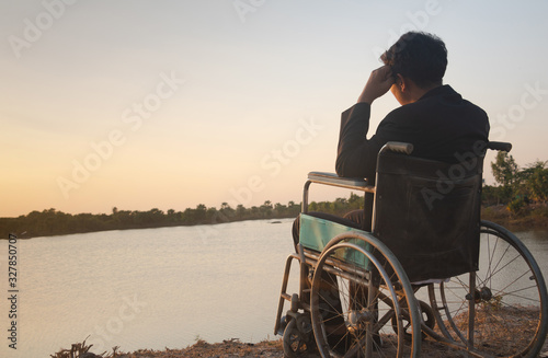 Young disabled man with blue sky background.He is alone and sitting on wheelchair.He is looking into river.despair,lonely,hope.Photo concept depression and Patient.