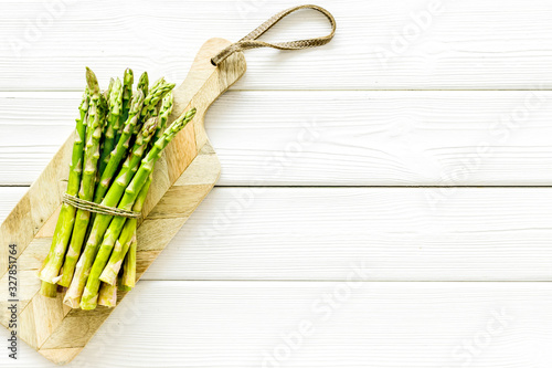 Cooking asparagus. Bunch steams on cutting board on white wooden background top-down copy space