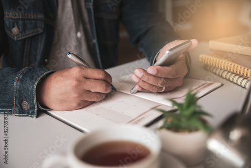 Calendar reminder event concept.Man hand planner or organizer writing on diary book and 2020 Calendar page.Student using mobile phone to plan appointment and schedule day photo