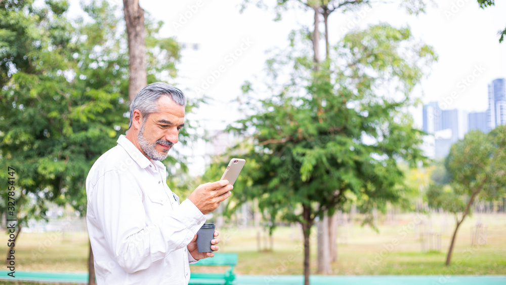 Portrait of happy handsome older man using smartphone for business or social media, Attractive mature business men in casual lifestyle checking his phone while walking at park, banner with copy space Portrait of happy handsome older man using smartphone for business or social media, Attractive mature business men in casual lifestyle checking his phone while walking at park, banner with copy space