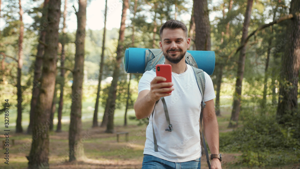 Handsome man with beard and backpack in forest uses speak on phone camera show around gps application orientation tourist travel hike lost sun communication telephone slow motion Handsome man with beard and backpack in forest uses speak on phone camera show around gps application orientation tourist travel hike lost sun communication telephone slow motion