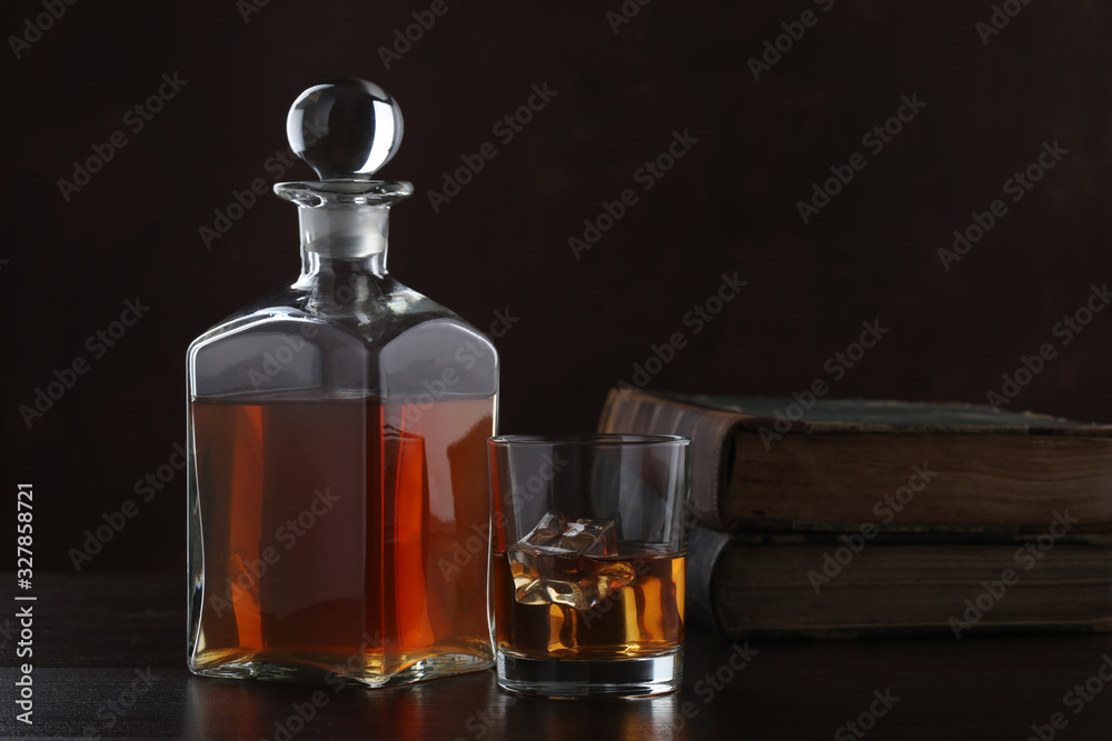 Bottle of whiskey with glass and old books on brown background