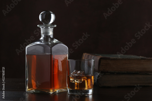 Bottle of whiskey with glass and old books on brown background