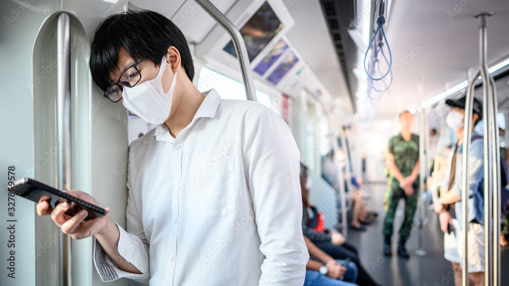 Asian man wearing surgical face mask using smartphone on skytrain or urban train. Wuhan coronavirus (COVID-19) outbreak prevention in public transportation. Health awareness for pandemic protection Asian man wearing surgical face mask using smartphone on skytrain or urban train. Wuhan coronavirus (COVID-19) outbreak prevention in public transportation. Health awareness for pandemic protection