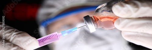 фотографія Doctor wearing protective suit gloves and mask filling up syringe