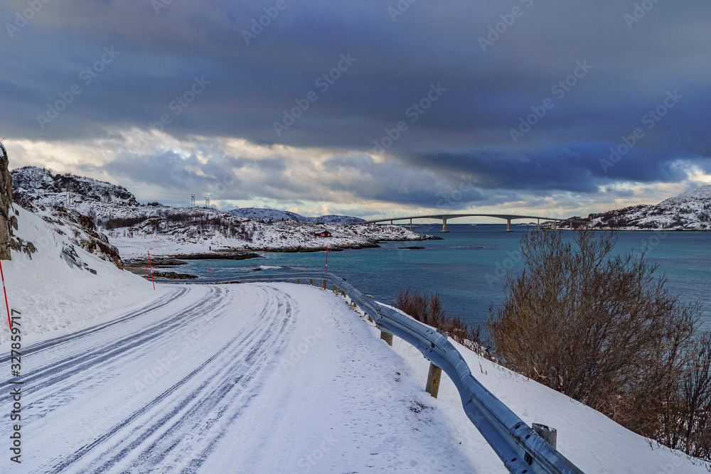 the snowstorm darkened the sky above the sommaroy bridge in norway on a turquoise blue sea with the snowy road the snowstorm darkened the sky above the sommaroy bridge in norway on a turquoise blue sea with the snowy road