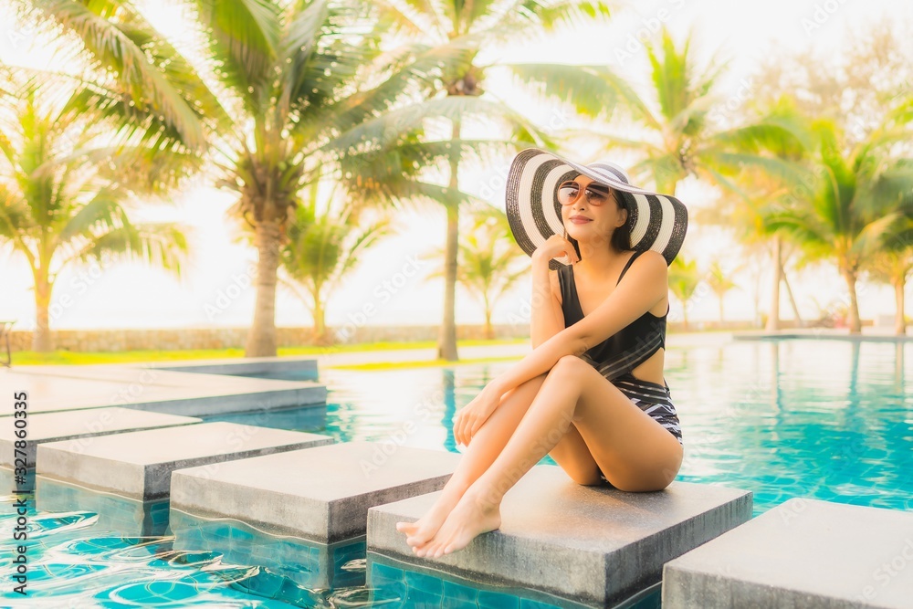 Portrait beautiful young asian woman relax around outdoor swimming pool in hotel resort with palm tree at sunset or sunrise