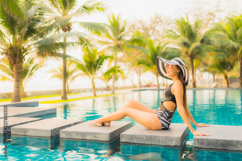 Portrait beautiful young asian woman relax around outdoor swimming pool in hotel resort with palm tree at sunset or sunrise