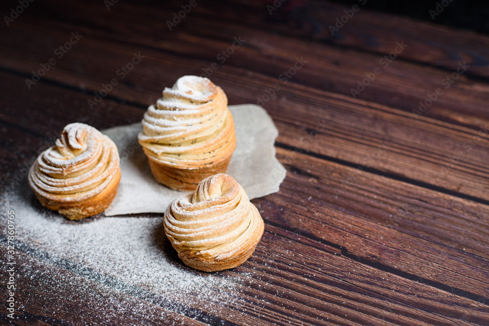 Modern trend baking 2020-cruffins puff muffin , a mixture of croissants and muffins. On a dark wooden table sprinkled with powdered sugar. Place to copy, view from above