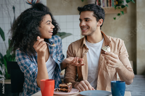 Happy multiracial friends communication together. Young lovely couple laughing, sitting in cafe. Beautiful African American woman and Indian man drinking coffee, eating tasty cake. First date concept