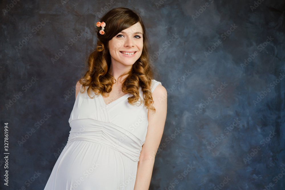 Happy pregnant girl smiling on dark artistic backdrop. Portrait of romantic beautiful European young woman wearing white dress. Happy pregnant girl smiling on dark artistic backdrop. Portrait of romantic beautiful European young woman wearing white dress.