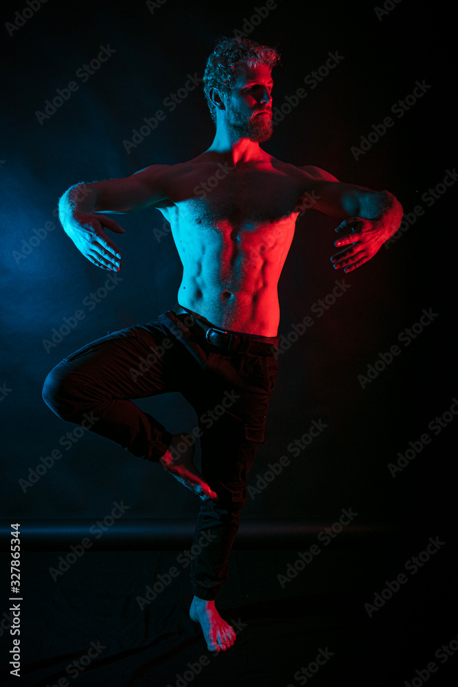 Man dancing ballet. Male wrestler posing. studio black-white background, red and blue lights.