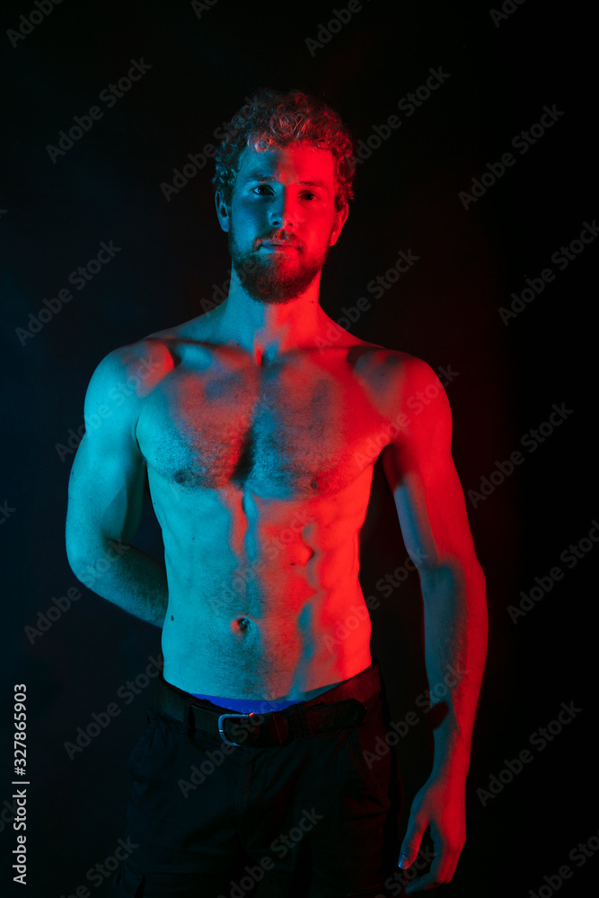 Fototapeta premium Male wrestler posing . studio black-white background, red and blue lights.