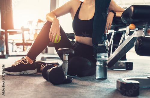 Woman exercise workout in gym fitness break and relax. Hands holding apple fruit after training sport with dumbbell and water bottle beside her.