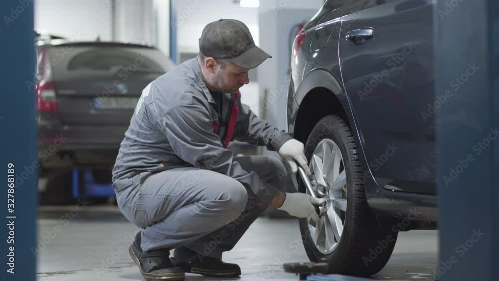 Side view of adult professional tightening screws on car wheel. Caucasian male auto mechanic working in auto repair shop. Occupation, lifestyle, automotive industry. Side view of adult professional tightening screws on car wheel. Caucasian male auto mechanic working in auto repair shop. Occupation, lifestyle, automotive industry.