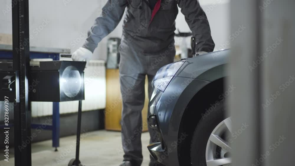 Unrecognizable male auto mechanic tightening screws in open car hood with screwdriver. Male professional maintenance engineer tuning or fixing vehicle in repair shop. Business, industry, lifestyle. Unrecognizable male auto mechanic tightening screws in open car hood with screwdriver. Male professional maintenance engineer tuning or fixing vehicle in repair shop. Business, industry, lifestyle.