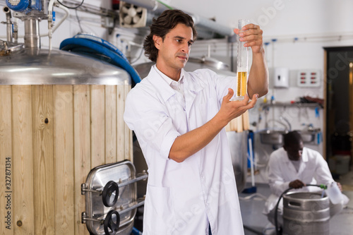 Young man expert is standing with flask for beer and analizying photo