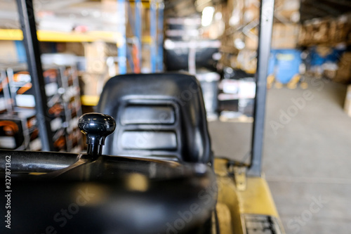 Shallow focus of a forklift truck's steering knob, helping the driver to make tight manoeuvres in a closed space. The empty drivers seat and warehouse is seen in the background.