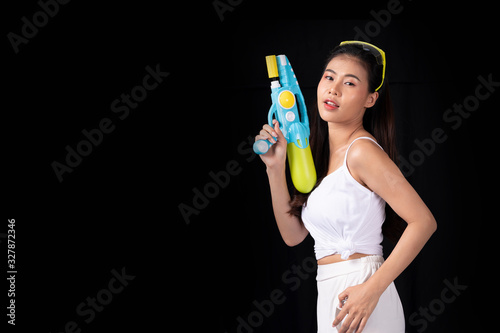 Portrait cheerful young asian woman with red glasses holding plastic water gun on balck background. Songkarn festival, Thailand. Thai New Year's Day. Isolated black background.