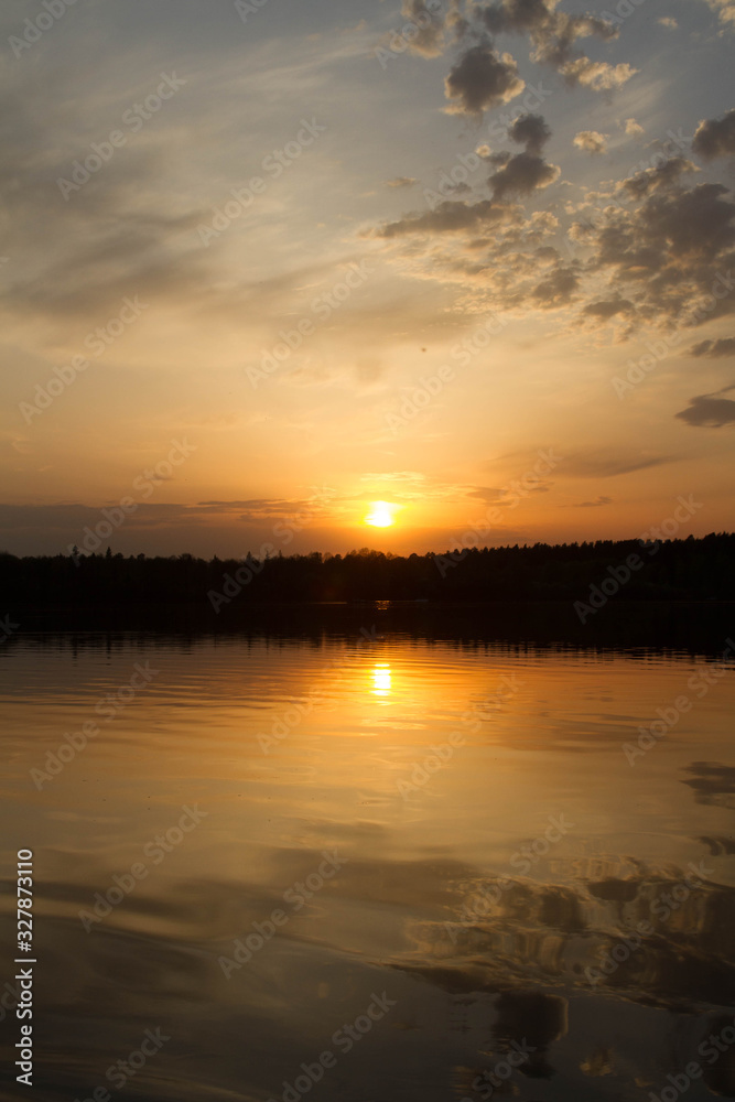 Fantastic bright sunset sky above the water surface. Perfect symmetrical reflection. Black silhouette of forest 