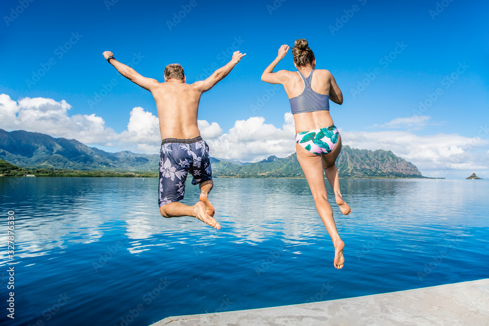 Man and women jumping together into the ocean while on a beautiful scenic Hawaiian vacation. Thrilling and exciting experience. Concept about holiday, success, accomplishment and lifestyle