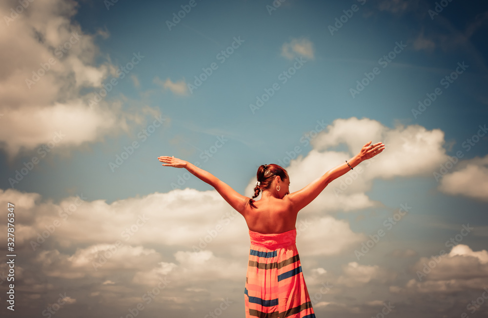 Rear view of carefree woman with arms outstretched against the sky. Rear view of carefree woman with arms outstretched against the sky.