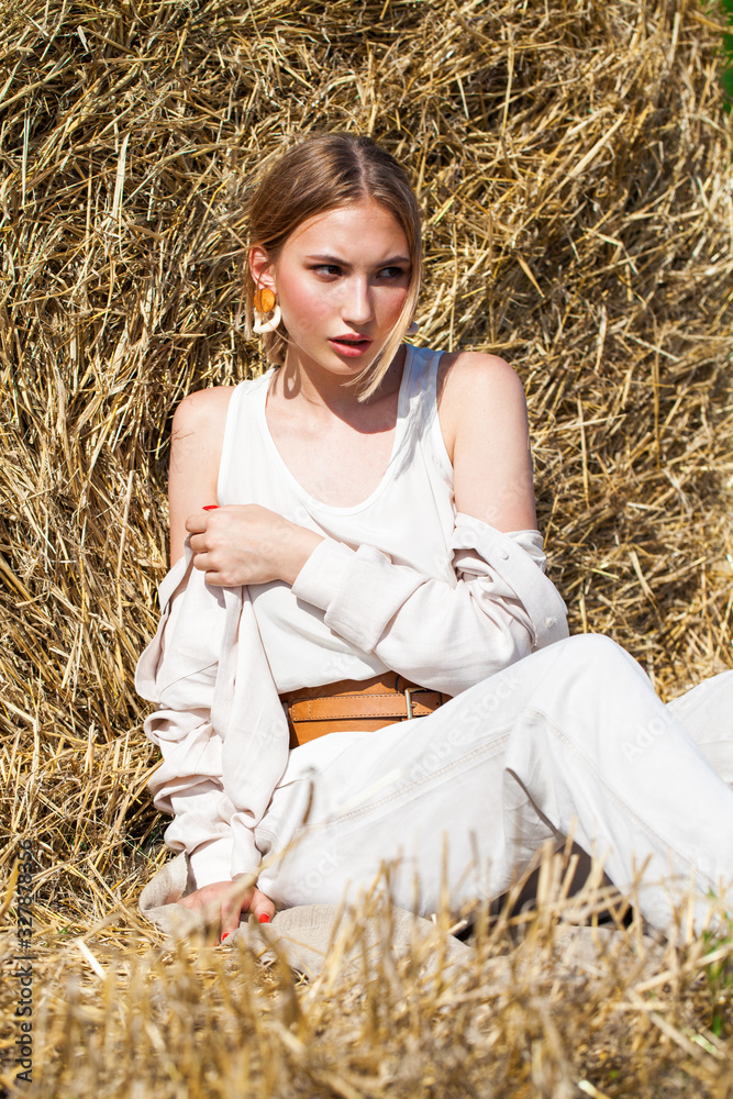 Young woman in a beige suit posing on a background of haystacks in a cut field. Young woman in a beige suit posing on a background of haystacks in a cut field.
