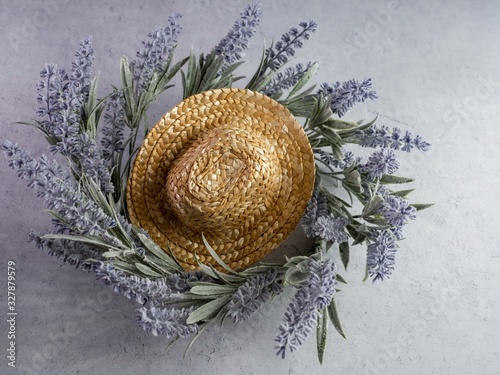 Lay flat photography of a straw cowgirl or cowboy hat sitting on top of a purple lavender flower plant wreath against a white gray plaster background.  Simple rustic country home decor.